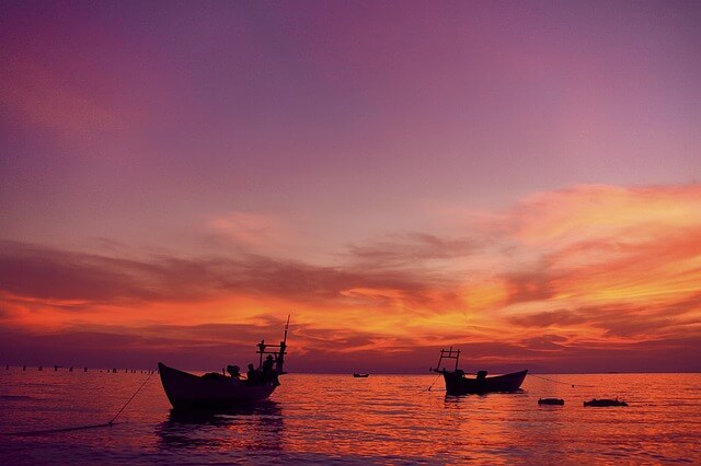 In this photo there are two simple fishing boats anchored out in the water. With no people in them they look lonely. The sky is filled with a beautiful display of yellows, oranges, pinks, purples, and reds, which are then reflected in the water below. Is this a sunrise or sunset? I don't know. But that's the point, isn't it?