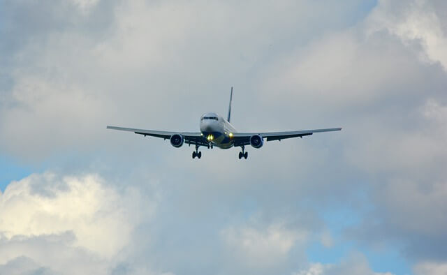 Silver blue plane, landing gear out and locked, against a sky of grey-white foggy clouds with a little bit of sunny blue peeking through.